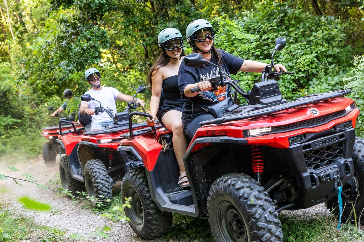 Zwei lachende Fahrerinnen teilen sich ein Quad auf einem Waldweg